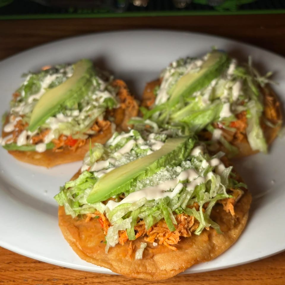 Three Tequila's 55 sopes topped with shredded chicken, lettuce, avocado, and crema on a white plate.