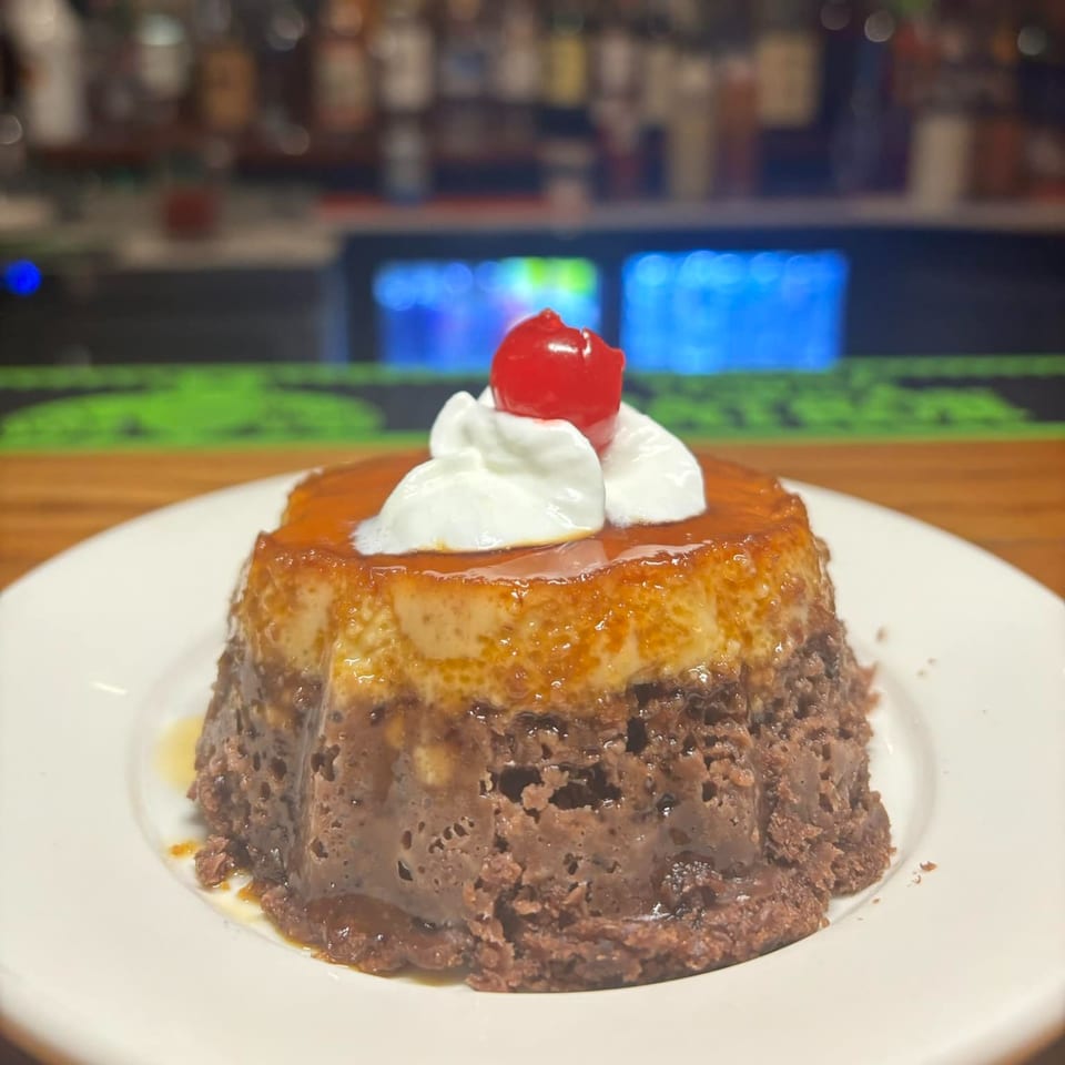 Mexican chocolate flan dessert topped with whipped cream and a cherry, on a white plate.