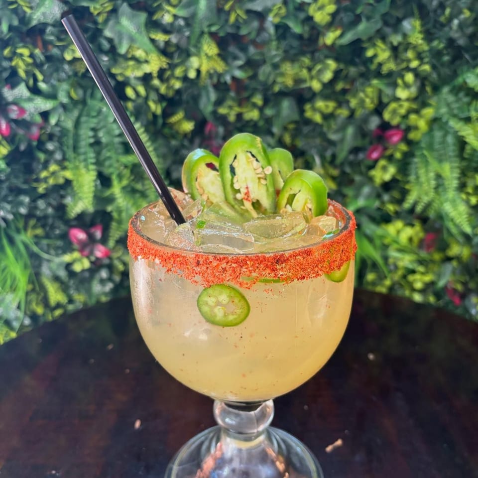A Tequila's 55 margarita with a chili-salted rim, jalapeño slices, and a black straw.