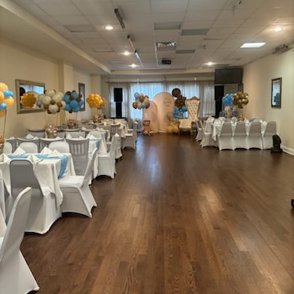 A large event room with tables set for a party, decorated with blue and gold balloons.