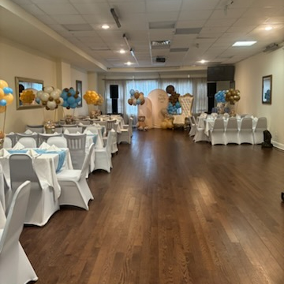 A large event room with tables set for a party, decorated with blue and gold balloons.