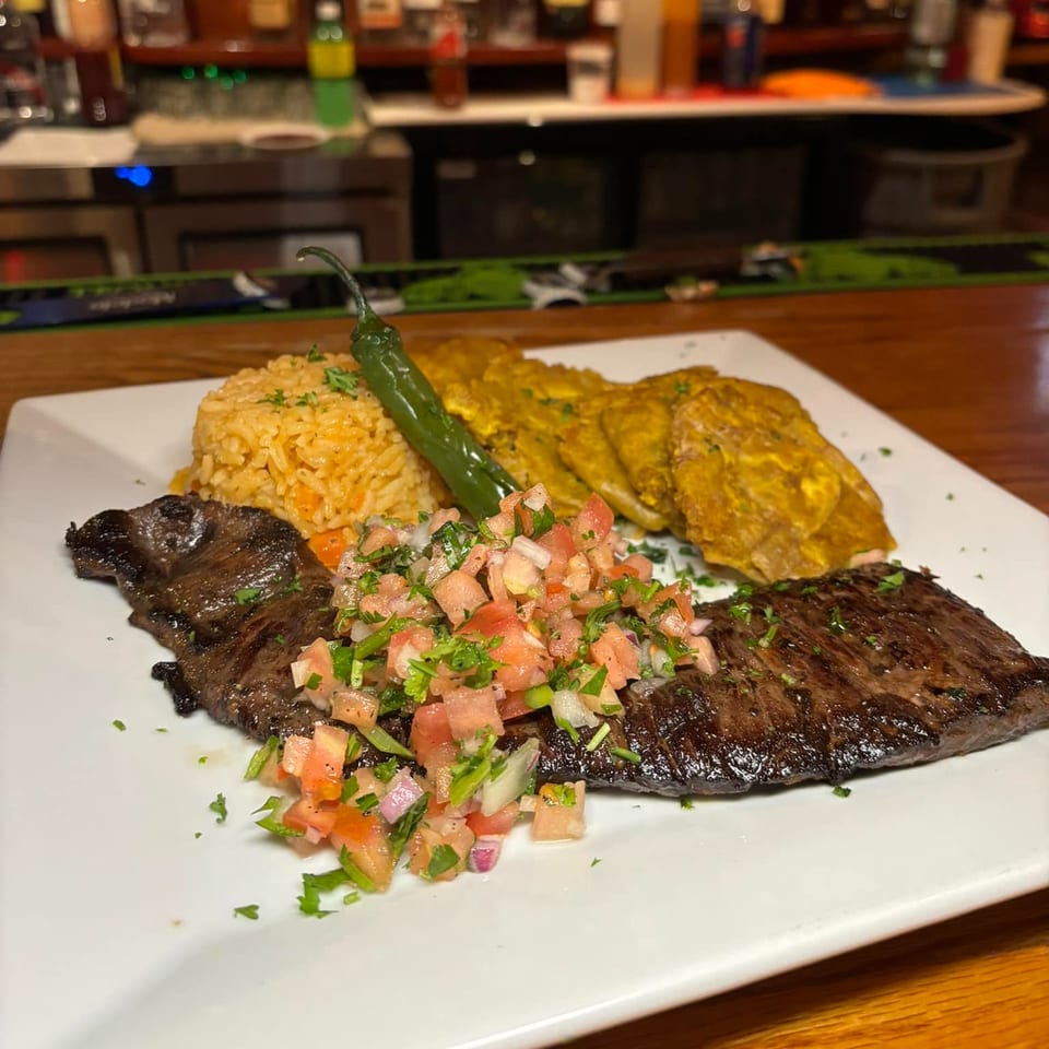 Grilled steak with pico de gallo, Mexican rice, fried plantains, and a green chili on a white plate.