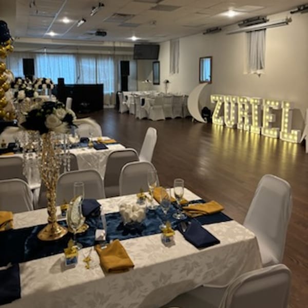 A large event room with tables set for a party, featuring blue and gold decor and illuminated letters.