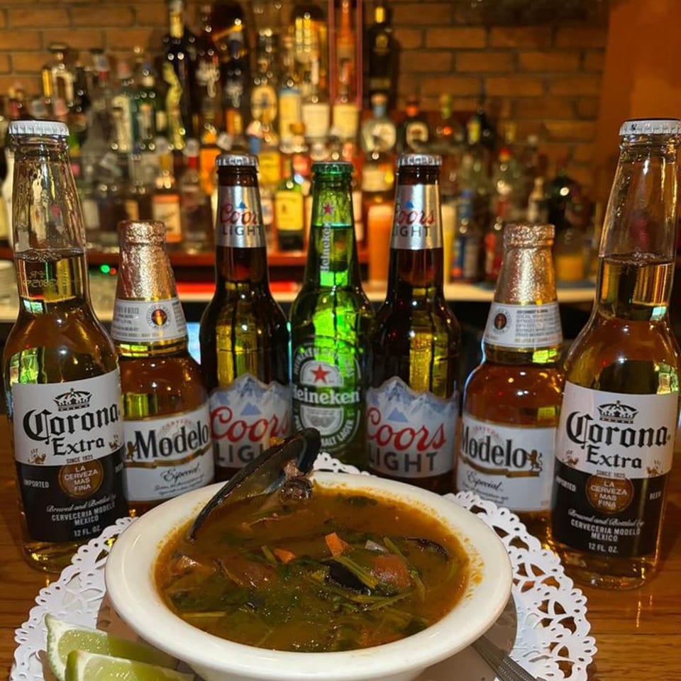 A bowl of seafood soup with lime wedges, surrounded by various beer bottles at Tequila's 55.