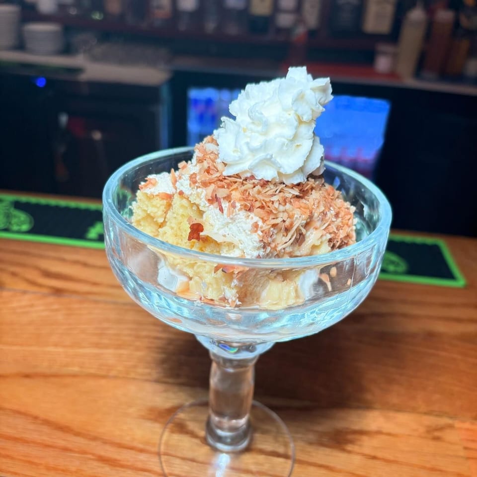 Tequila's 55 tres leches cake with whipped cream and toasted coconut flakes in a glass.