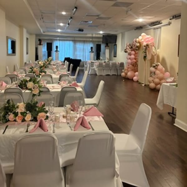 A long dining room with tables set with pink napkins and floral centerpieces, and balloon arches.