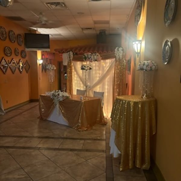 A decorated event space at Tequila's 55 with gold tablecloths, floral arrangements, and string lights.