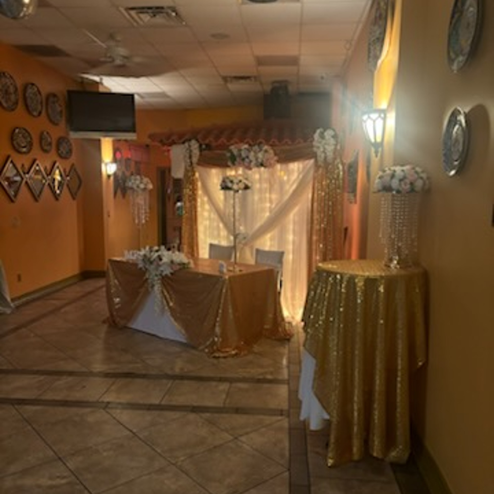 A decorated event space at Tequila's 55 with gold tablecloths, floral arrangements, and string lights.