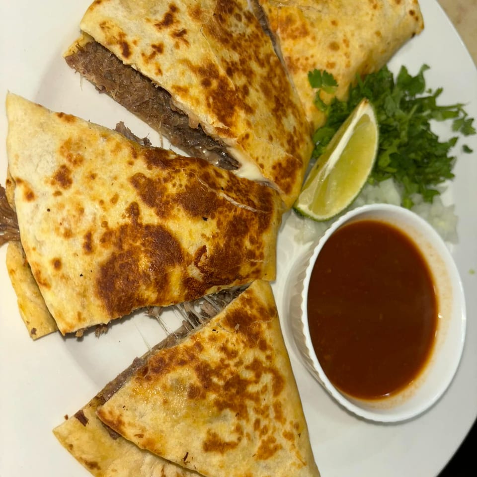 Tequila's 55 birria quesadillas with cilantro, lime, and a side of consommé on a white plate.