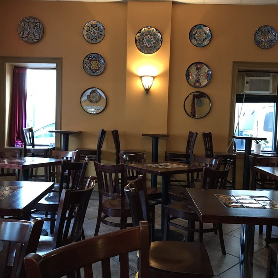Interior of Tequila's 55 restaurant with empty tables, chairs, and decorative plates on mustard-yellow walls.