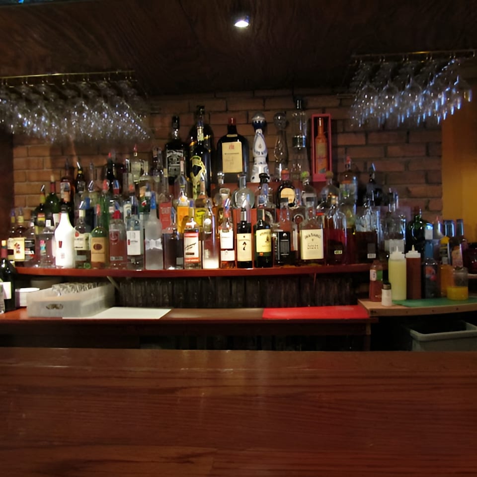 A well-stocked bar with various liquor bottles, hanging glasses, and brick wall background at Tequila's 55.